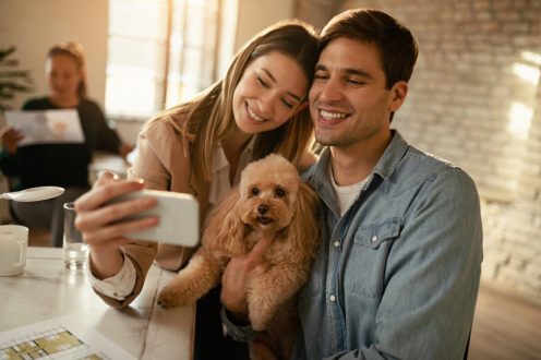 Young smiling coworkers and their dog taking selfie in the offic